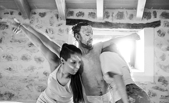 Three dancers emerge, dressed in the color of stone